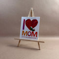 Book titled 'I Love Mom with The Very Hungry Caterpillar' on a small wooden easel against a beige background