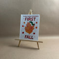 Children's book titled 'The Very Hungry Caterpillar's First Fall' on a small wooden easel against a neutral background