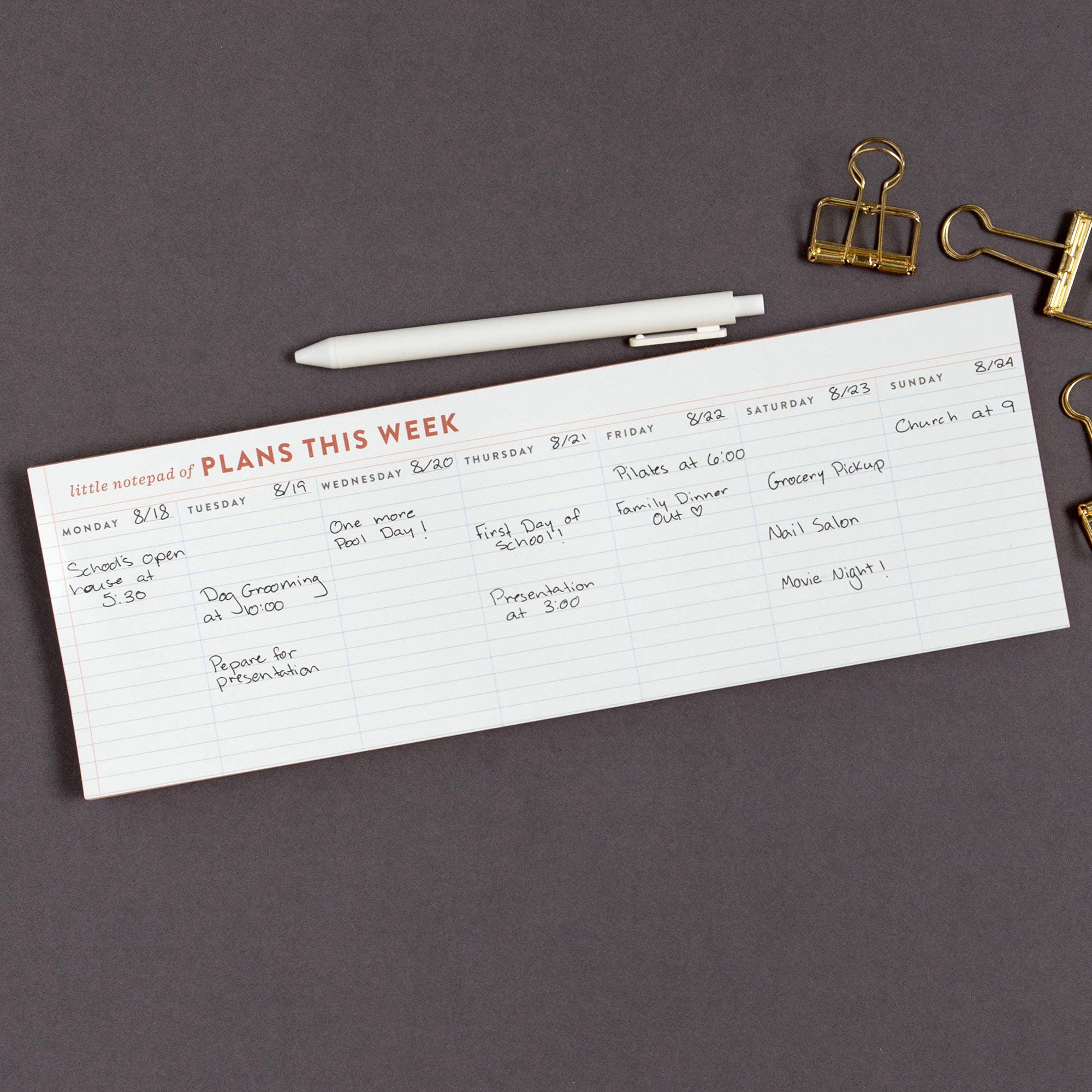 Weekly planner sheet with handwritten tasks on a dark surface with office supplies.