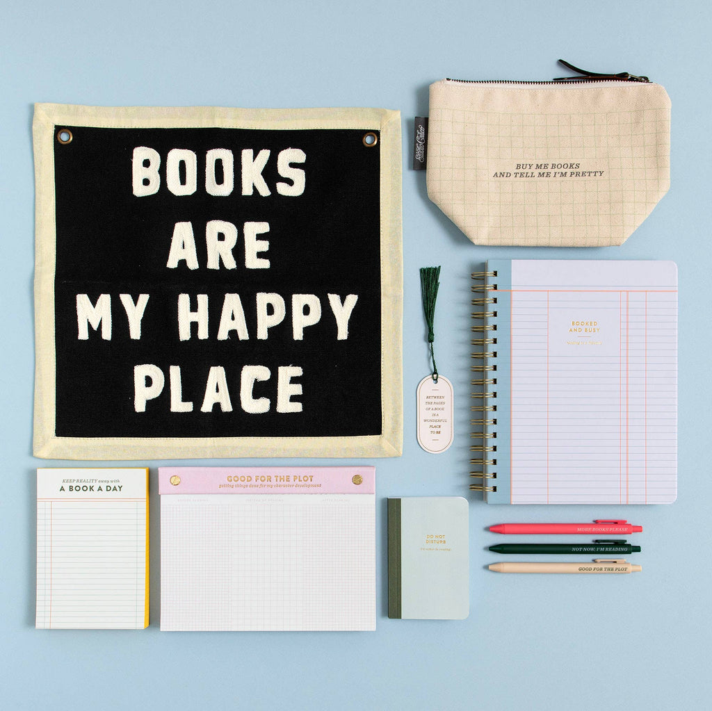 Collection of stationery items including a sign with 'Books are my happy place', notebooks, and pens on a light blue background.