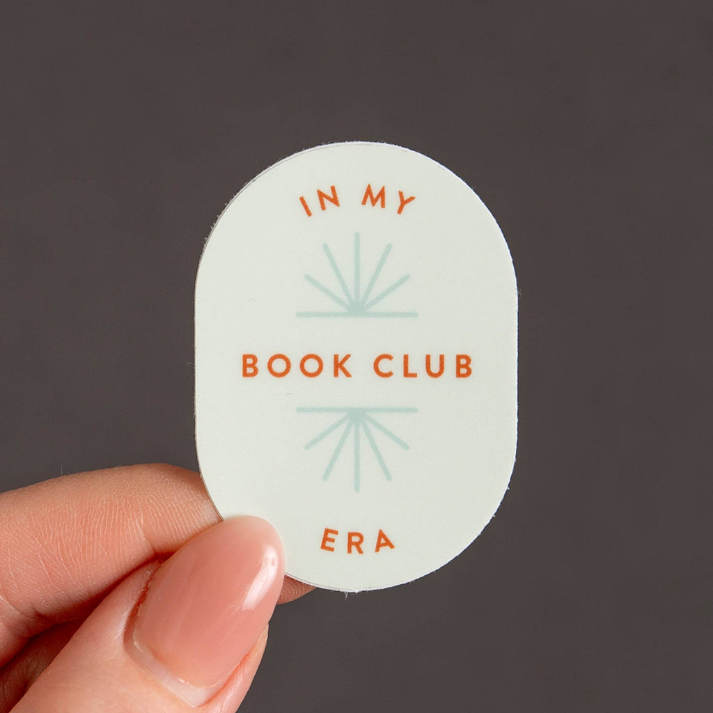 Sticker with 'In My Book Club Era' text held by a hand against a dark background