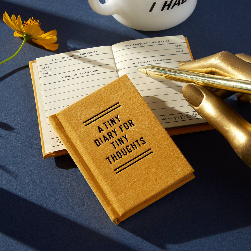 Tiny diary for tiny thoughts with gold pen, yellow flower, and cozy journaling setup on blue background